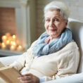 Portrait of smiling attractive retired woman in beige cardigan distracted for second from reading book in order to pose for photography